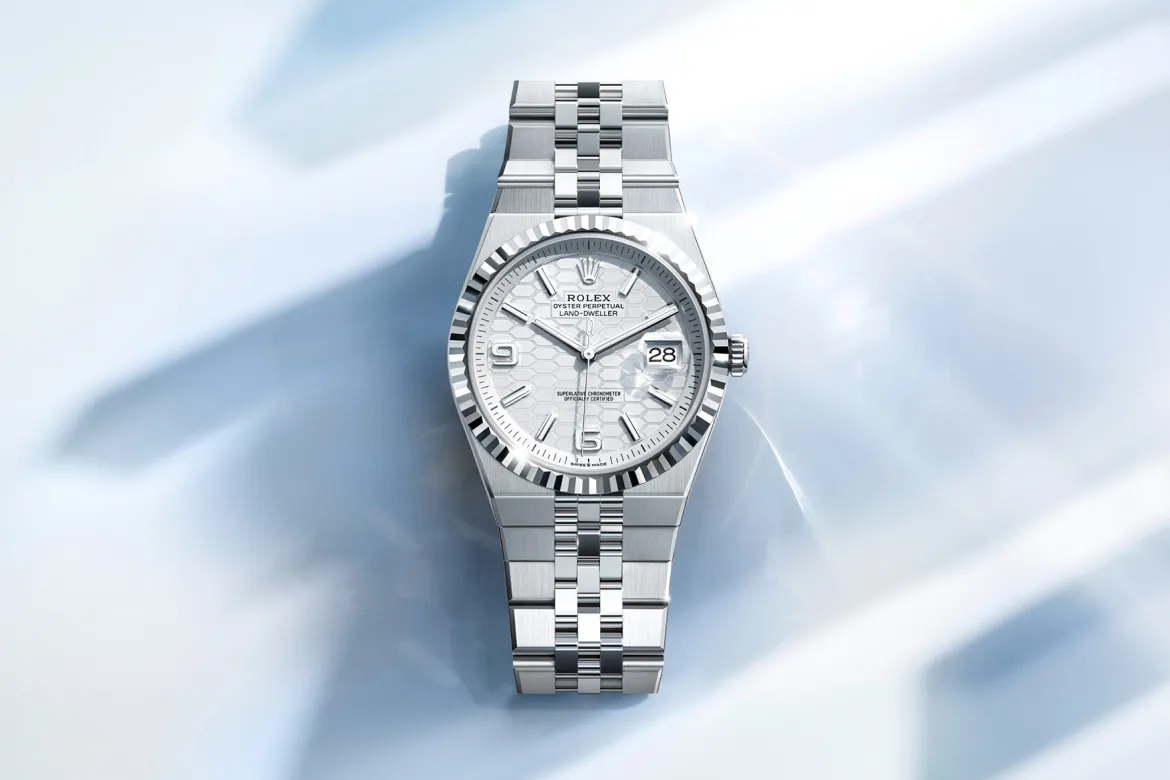 Close-up of a stainless steel Rolex watch with a fluted bezel and date window on a pale blue background.