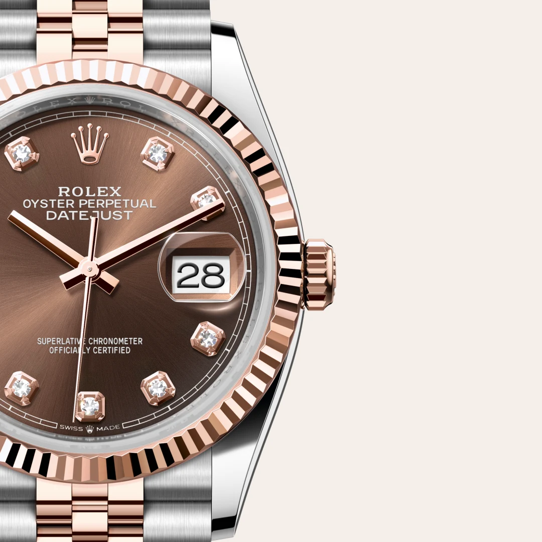 Close-up of a rose-gold Rolex Datejust watch face with diamond hour markers and the date window showing 28. | Brela