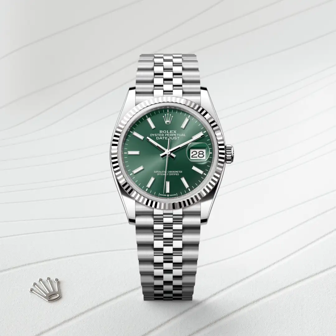Rolex Datejust wristwatch with green dial, fluted silver bezel, and Jubilee metal bracelet on a light striped surface. | Brela