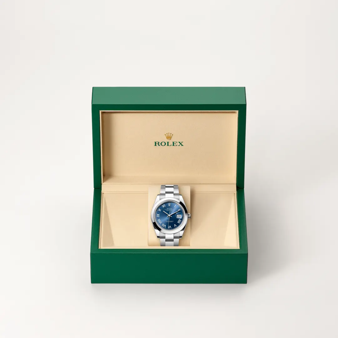 Rolex wristwatch with blue dial displayed in an open green presentation box with a beige interior. | Brela