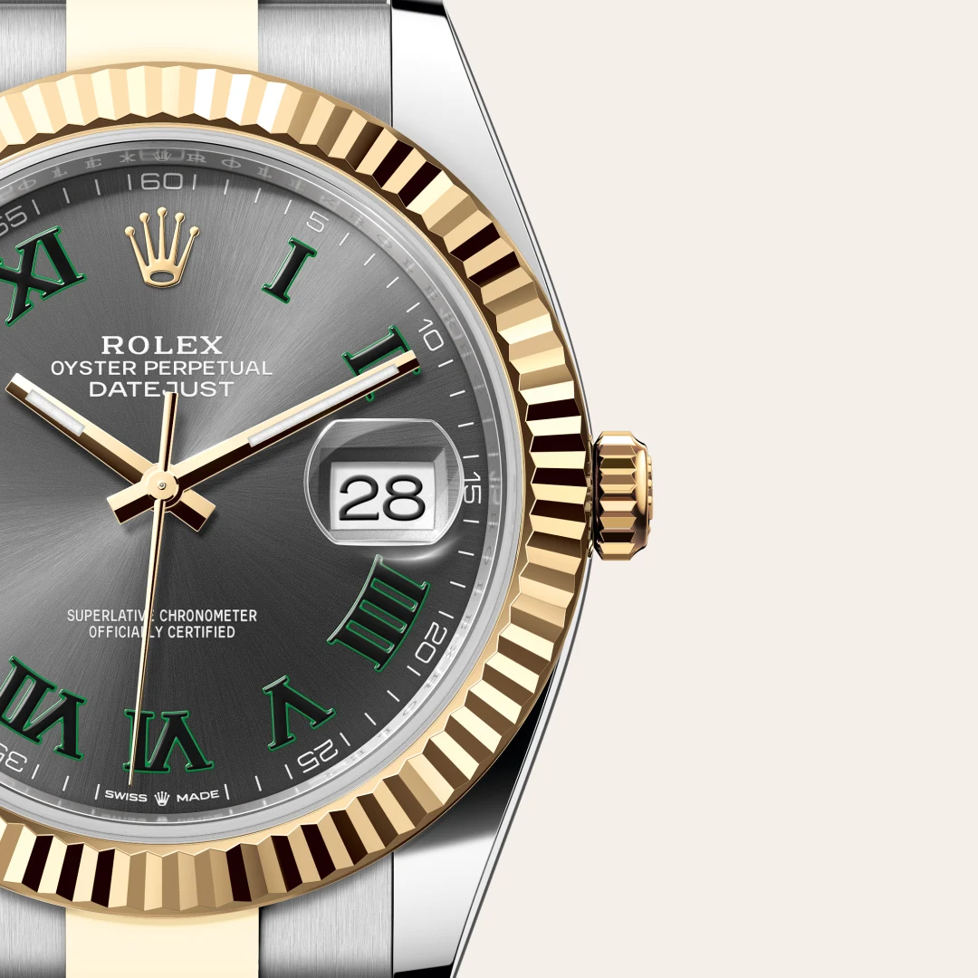 Close-up of a two-tone Rolex DateJust watch face with a gold fluted bezel, green Roman numerals, and date window showing 28 | Brela