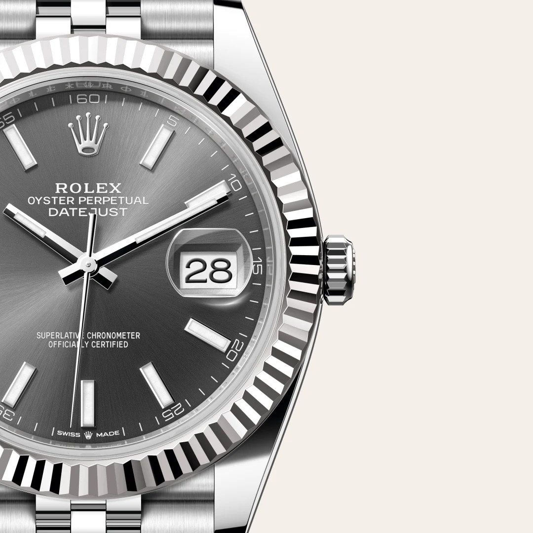 m126334-0014-slide3 | Brela Close-up of a stainless steel Rolex Oyster Perpetual Datejust watch with a black sunburst dial, silver markers and hands, date window at 3 under a magnifier, and a fluted bezel. | Brela