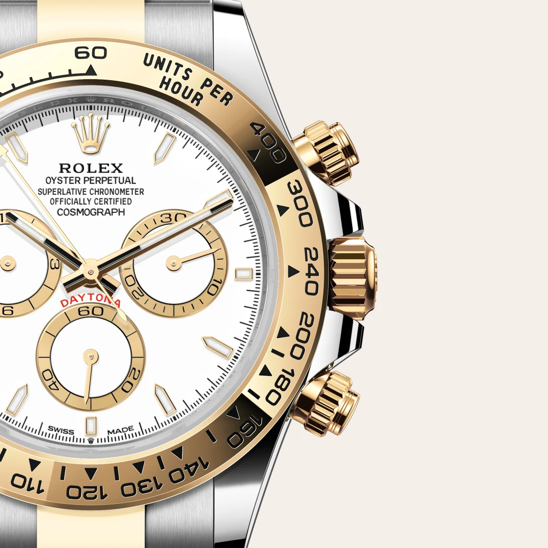 Close-up of a two-tone Rolex Daytona watch with a white dial, gold subdials, and a gold tachymeter bezel; crown and pushers visible on the right.
