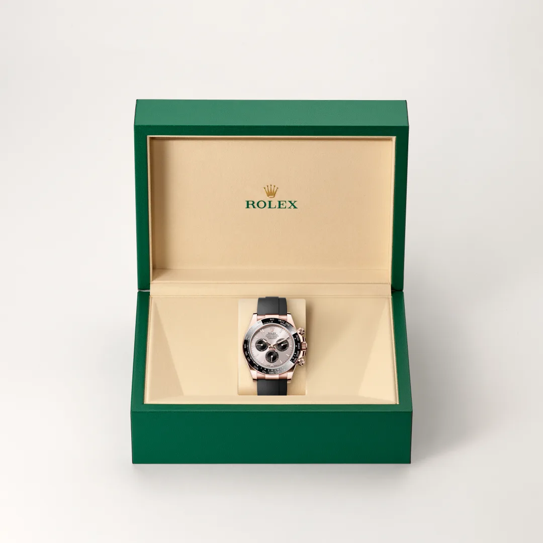 Rolex watch in its green presentation box with beige interior, facing forward showing its silver face and black strap. | Brela