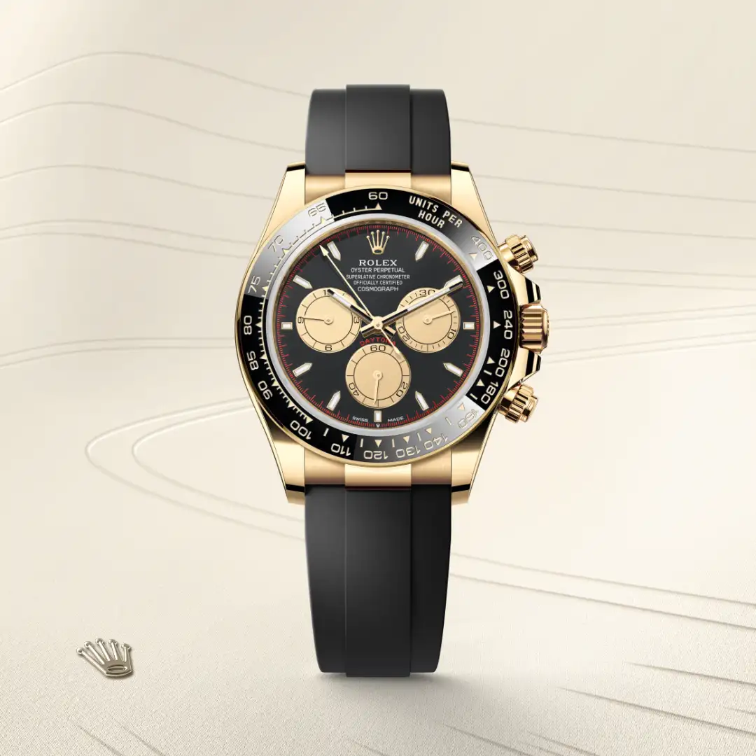 Gold Rolex chronograph with black dial, three subdials, and black strap on a light background. | Brela