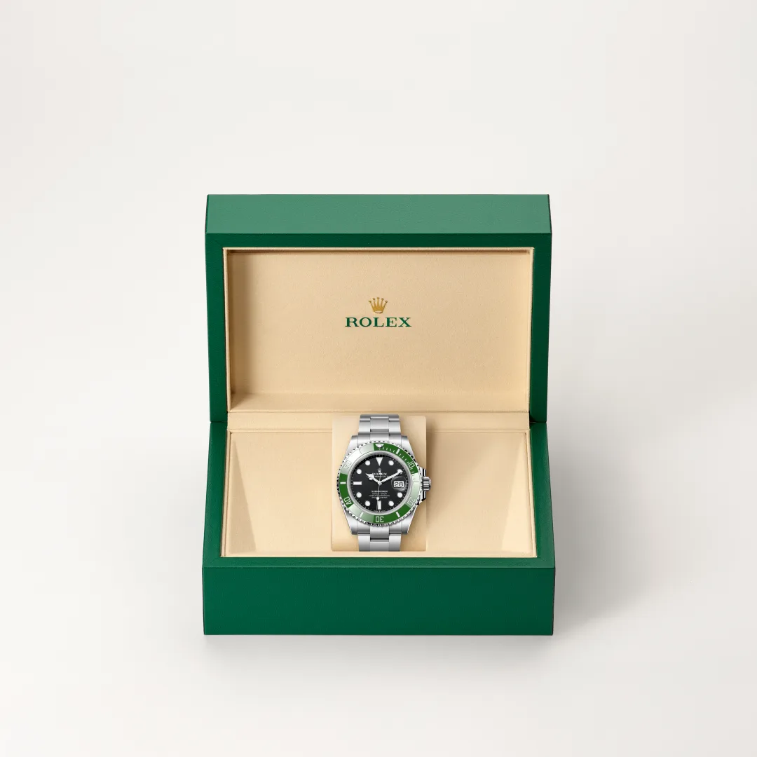 m126610lv-0002-slide2 | Brela Rolex wristwatch with black dial and green bezel, displayed in an open green presentation box with a beige interior. | Brela