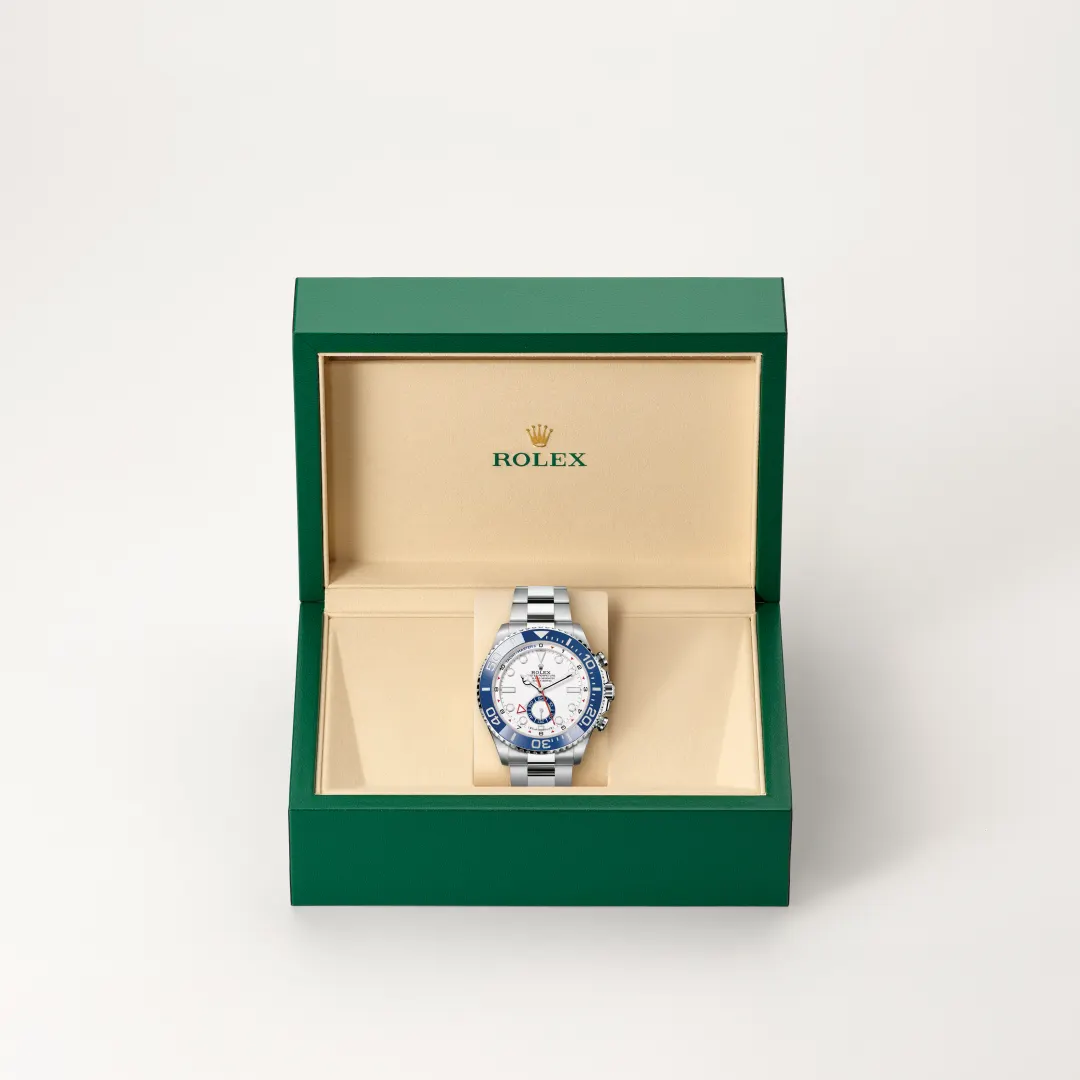 Open green Rolex box with beige interior displaying a silver Rolex watch with a blue bezel and white dial inside a padded holder