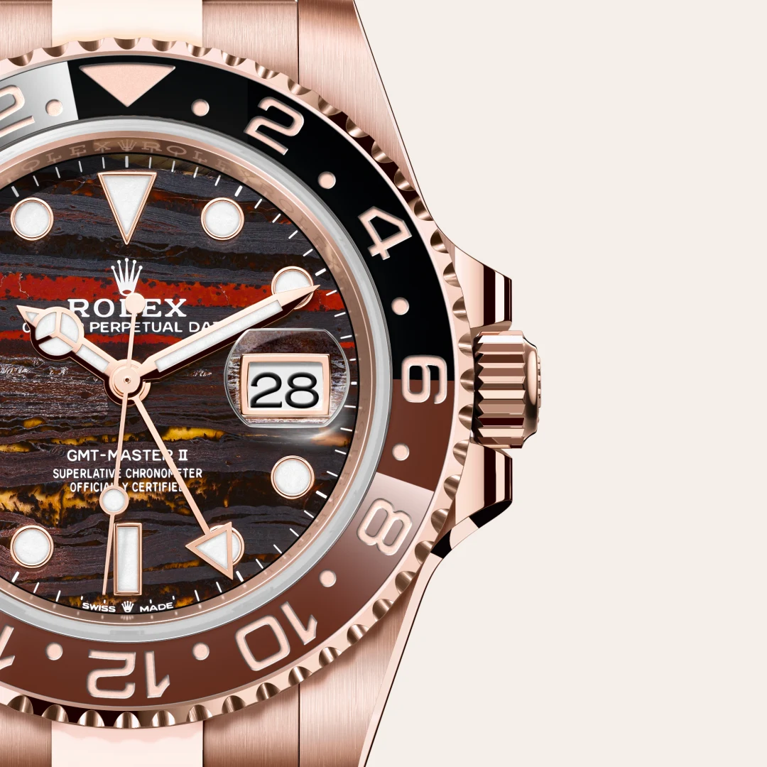 Close-up of a rose-gold Rolex GMT-Master II watch, showing a dark striped dial, white lume markers, and date window at 3 o'clock with magnifier. | Brela