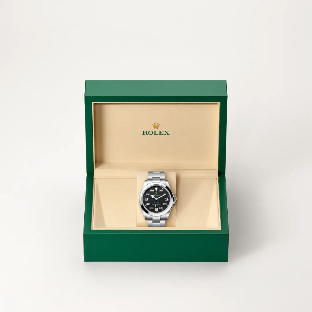 Rolex wristwatch in an open green box with beige interior and logo, silver bracelet and black dial showing time. | Brela