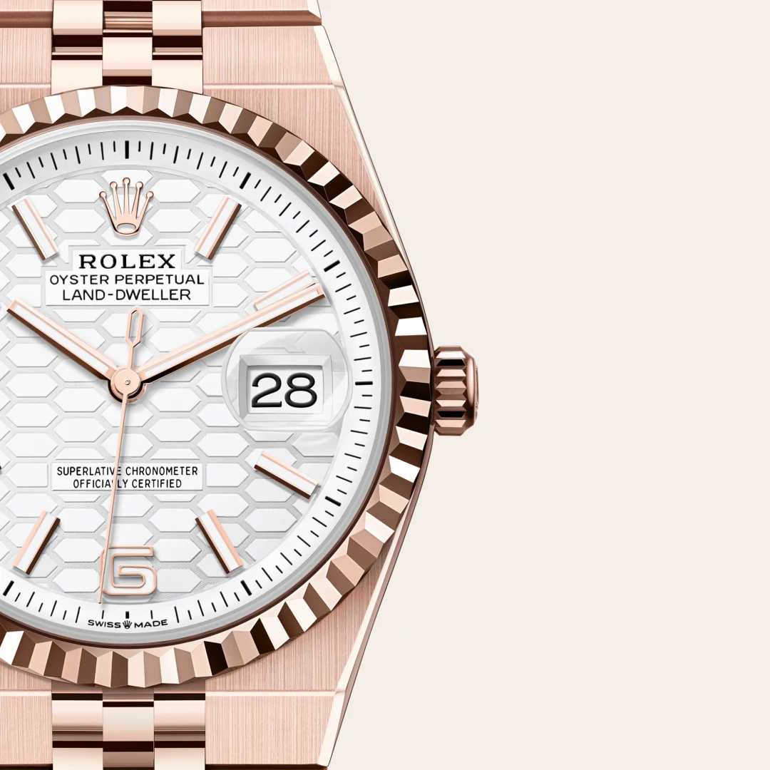 m127235-0001-slide3 | Brela Close-up of a rose‑gold Rolex Oyster Perpetual Land‑Dweller watch face with a white honeycomb dial, date window at 3, and fluted bezel. | Brela