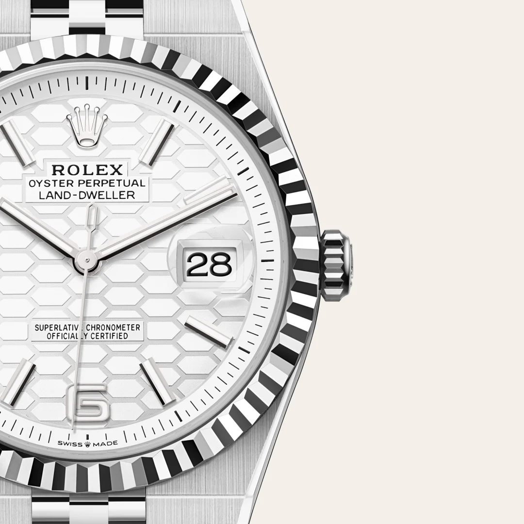 Close-up of a stainless Rolex watch face with date window showing 28, hexagonal dial pattern, fluted bezel, and crown. | Brela