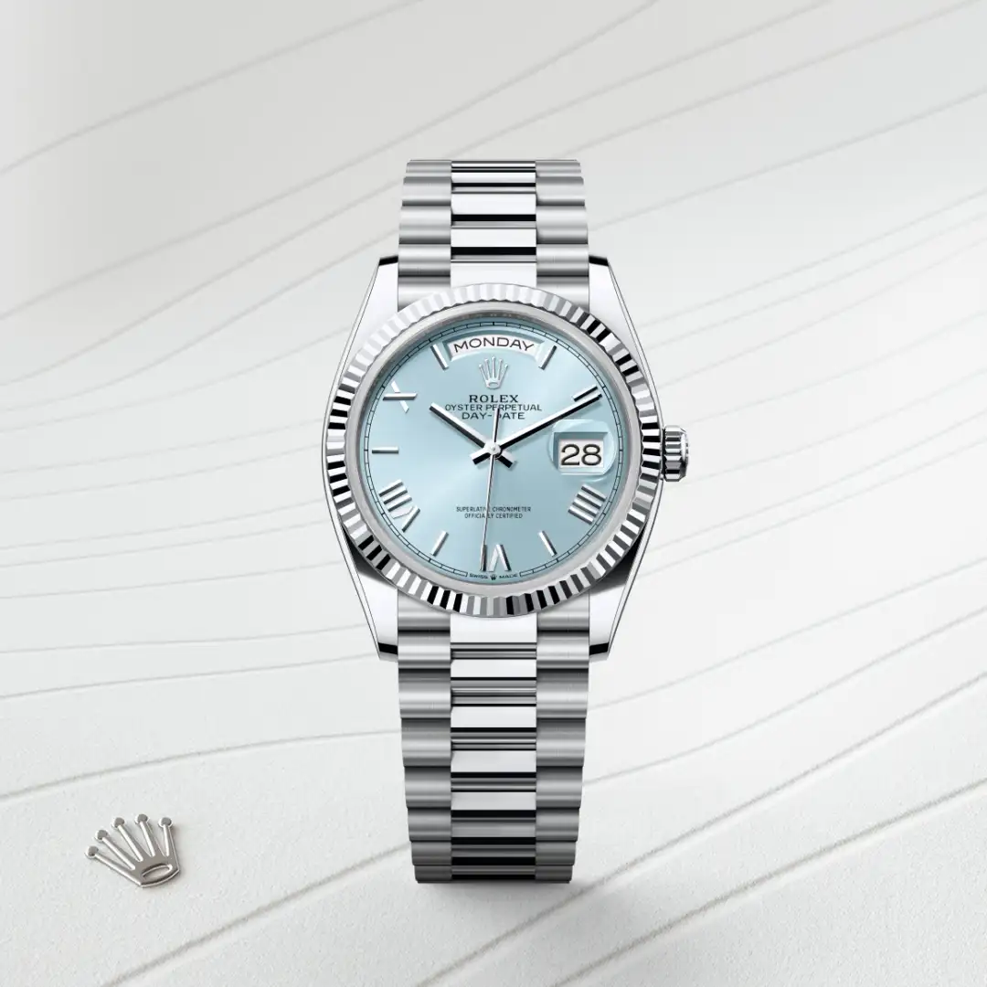 m128236-0018-slide1 | Brela Rolex Day-Date wristwatch with a pale blue dial, fluted bezel, and stainless steel bracelet displaying the day 'MONDAY' and date '28'. Their iconic crown logo is visible on the dial side, set against a light background. | Brela
