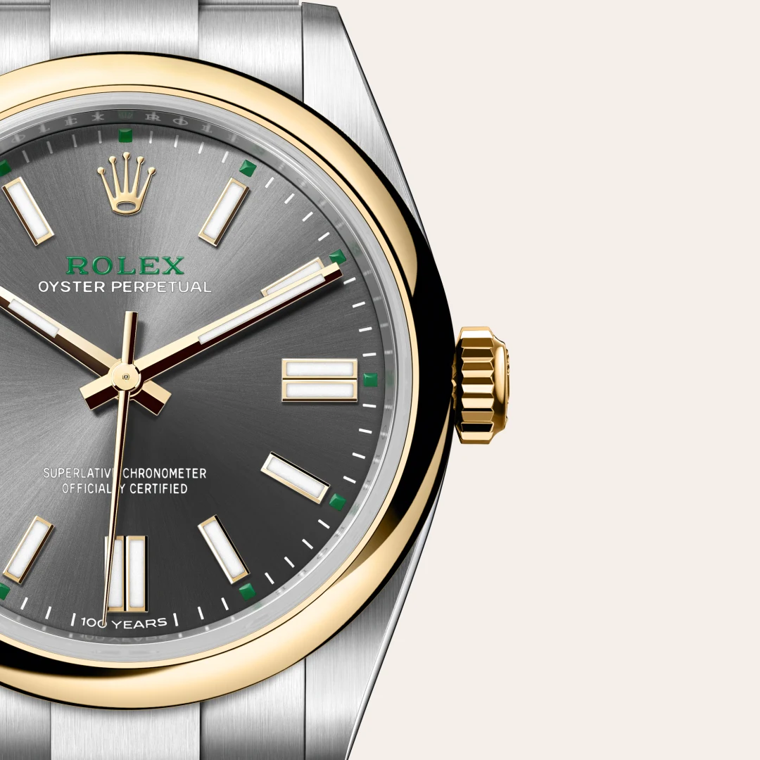 m134303-0001-slide3 | Brela Close-up of a Rolex Oyster Perpetual watch: grey sunburst dial, gold bezel and crown, and a two-tone metal bracelet visible on the left. | Brela