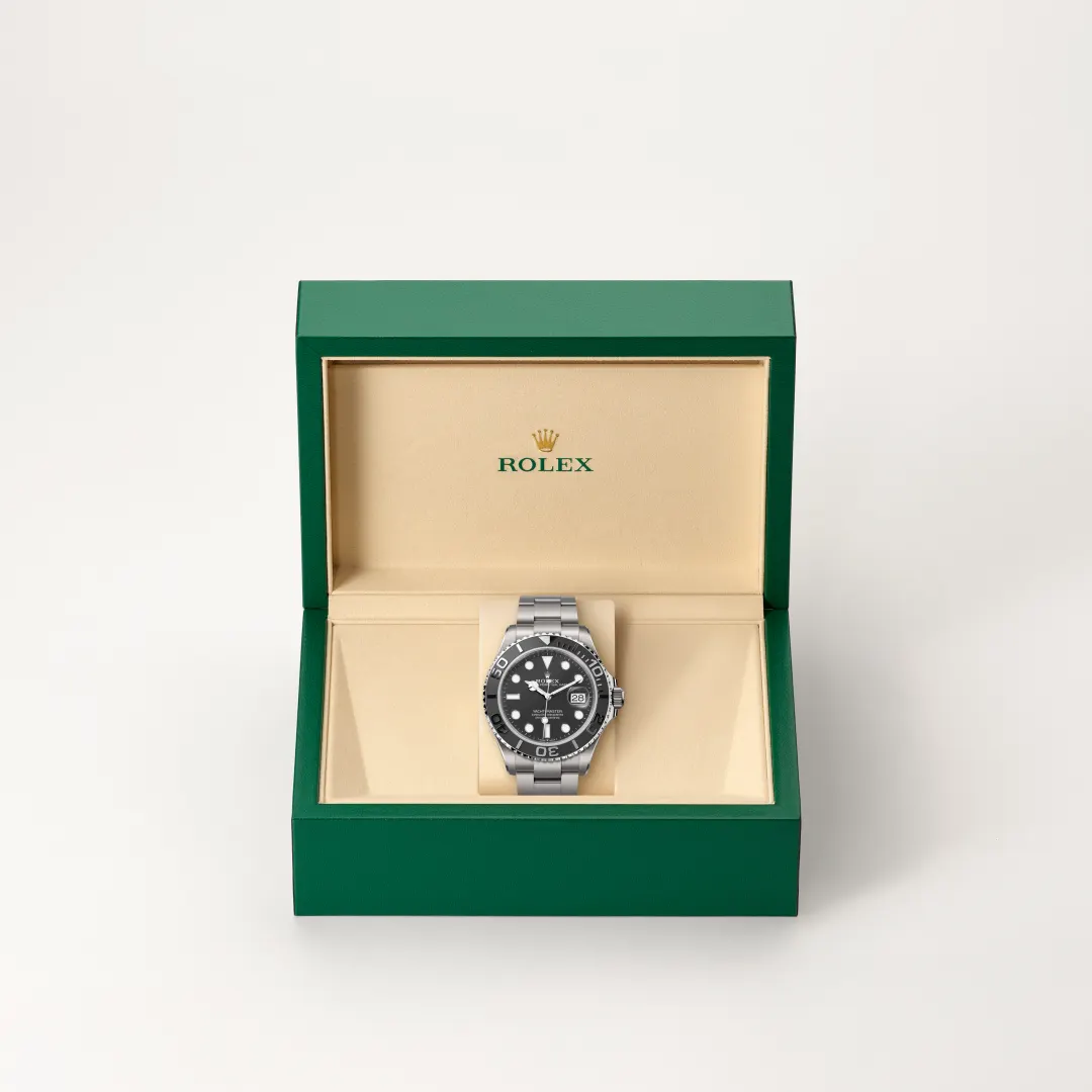m226627-0001-slide2 | Brela Rolex watch displayed in an open green box with beige interior, showcasing a black dial and metal bracelet. | Brela