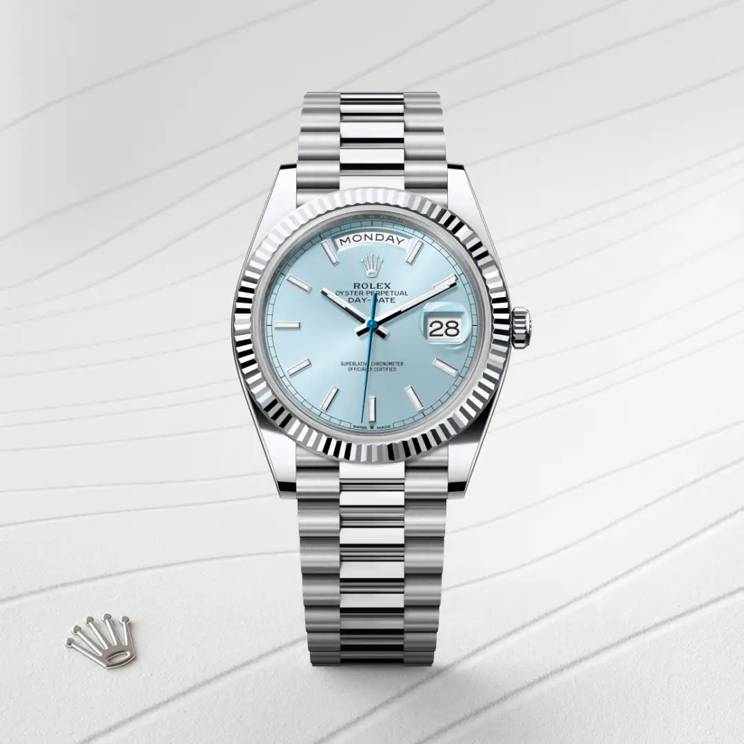 Rolex Day-Date wristwatch with a light blue dial and stainless steel bracelet displayed on a light striped surface, crown logo nearby | Brela