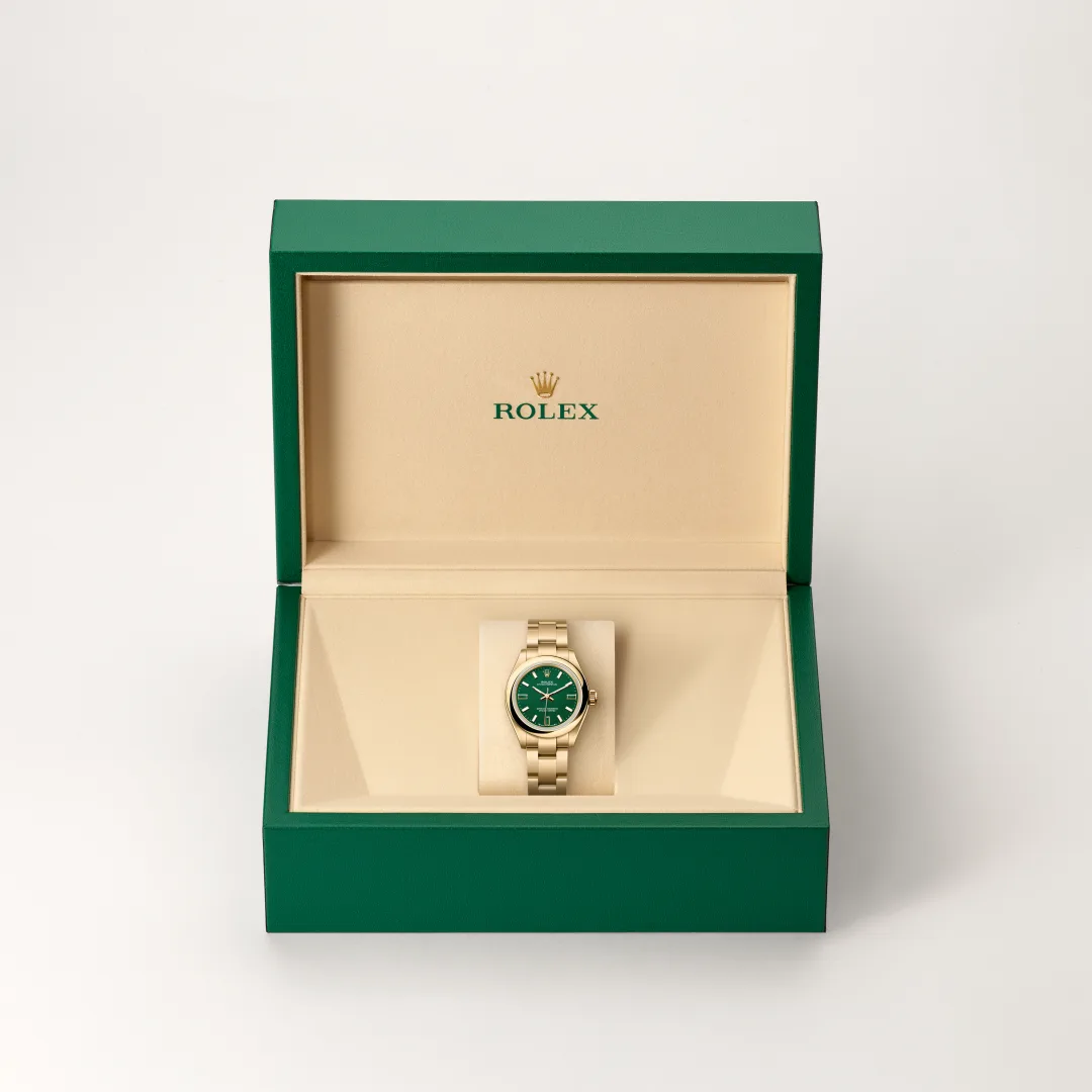 Gold Rolex wristwatch with a green dial in a beige interior, opened green presentation box showing the logo above. | Brela