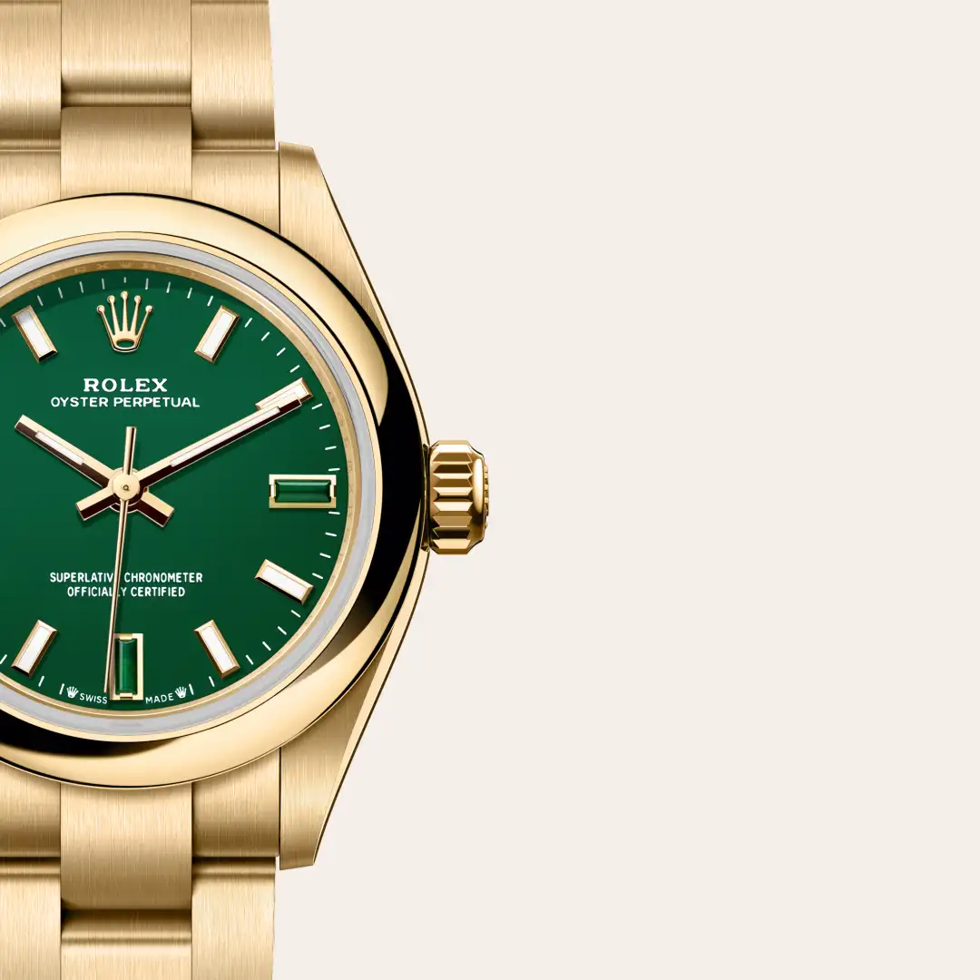 Close-up of a gold Rolex Oyster Perpetual wristwatch with a green dial and metal bracelet on a light background. | Brela