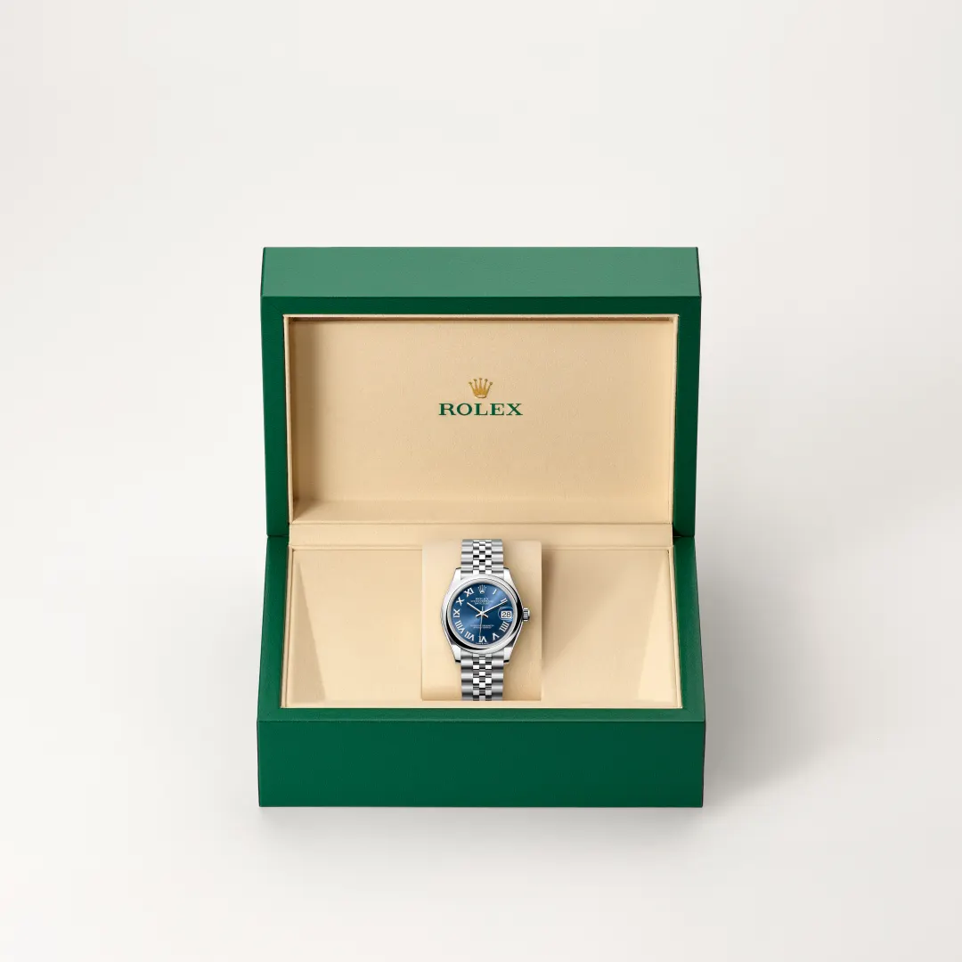 Green Rolex presentation box opened to reveal a stainless steel watch with a blue dial and date window on a beige insert | Brela