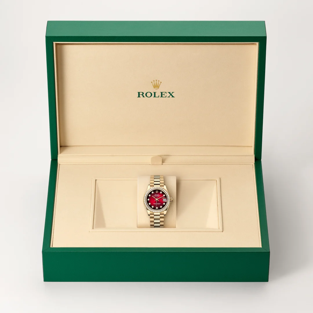 Open green Rolex presentation box reveals a gold Rolex watch with a red dial on a beige display cushion inside the box. | Brela