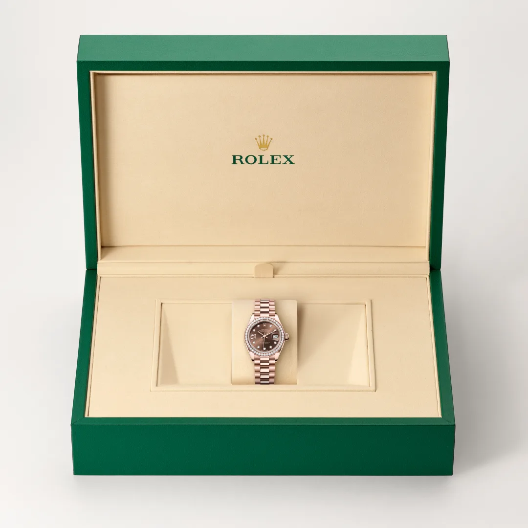 m279135rbr-0001-slide2 | Brela Rolex wristwatch in an open green presentation box, rose-gold bracelet and diamond bezel on a beige interior. | Brela