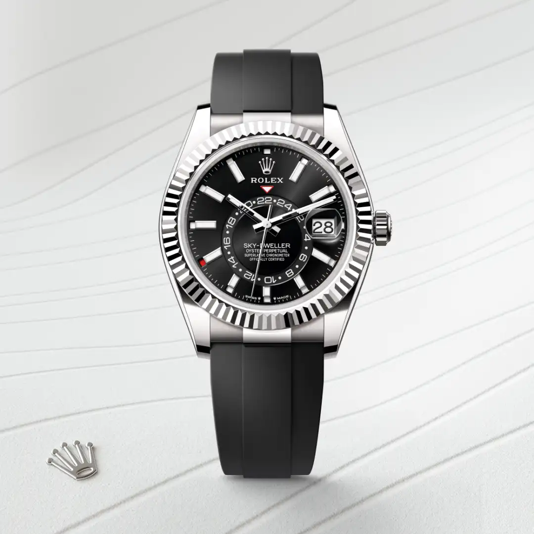 m336239-0002-slide1 | Brela Silver Rolex Sky-Dweller with black dial, fluted bezel, white hour markers, and black rubber strap on a pale striped background; date window at 3 o'clock visible on the dial. | Brela