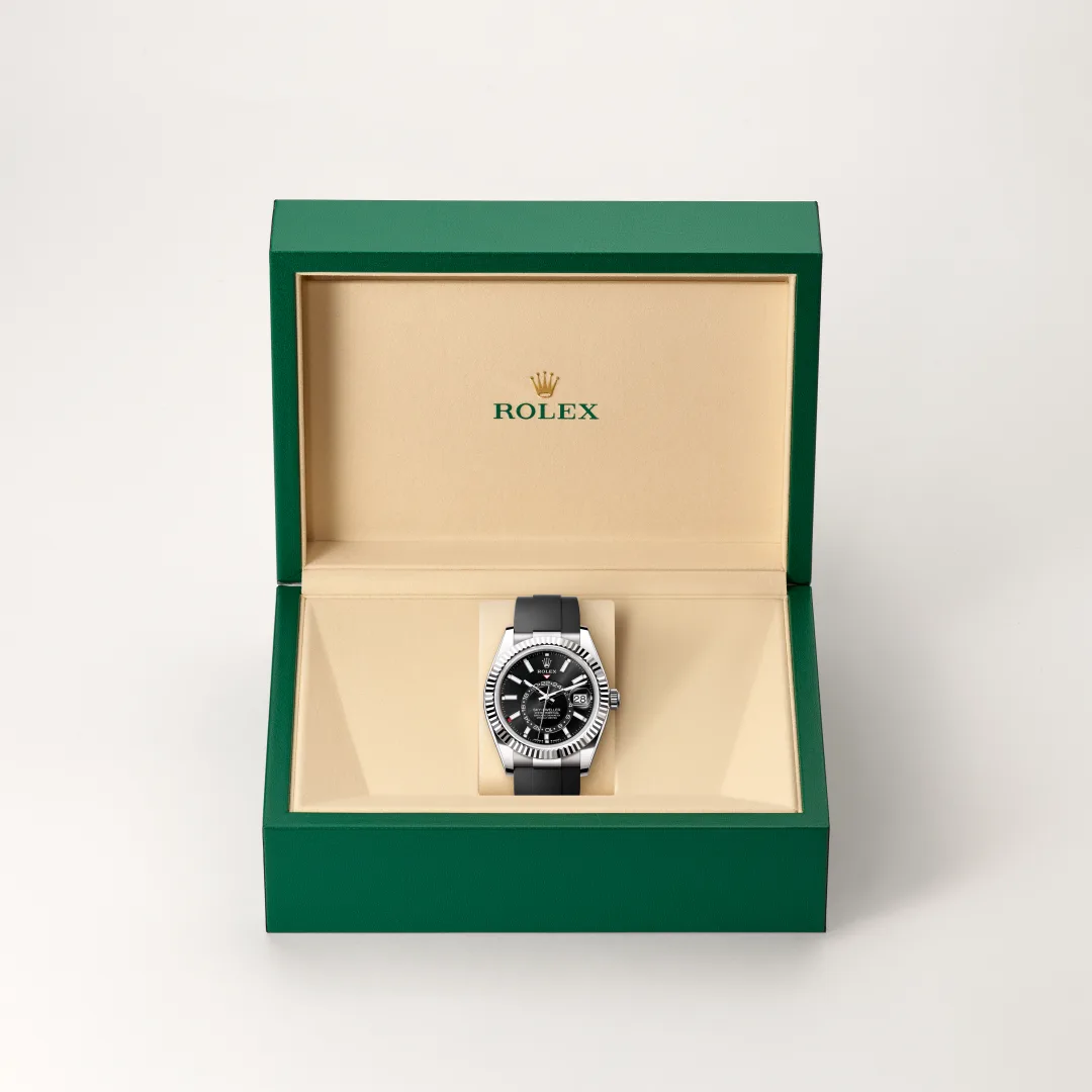 m336239-0002-slide2 | Brela Rolex wristwatch with black dial and silver bezel nestled in an open green presentation box with a beige interior. | Brela