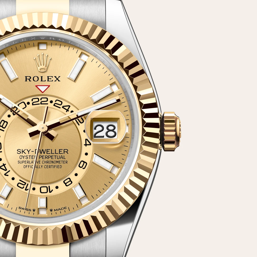 m336933-0001-slide3 | Brela Close-up of a gold Rolex Sky-Dweller watch dial with date window showing 28, fluted bezel, and gold crown against a light background. | Brela