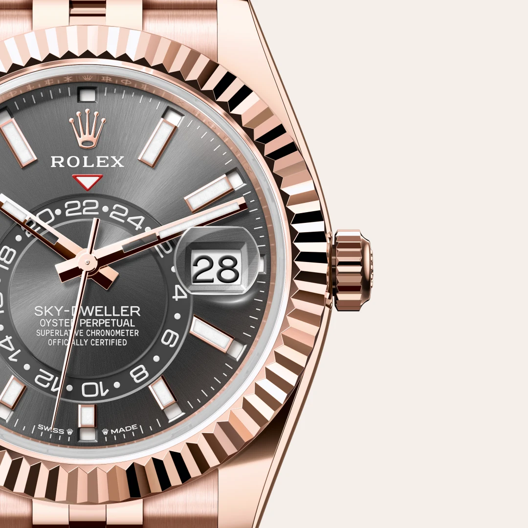Close-up of a rose-gold Rolex Sky-Dweller watch with a fluted bezel and dark gray dial showing date at 3 o'clock. | Brela