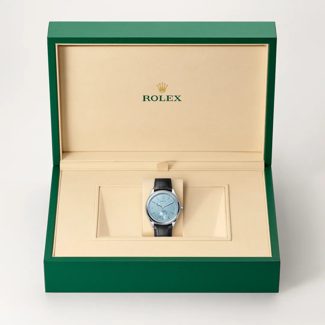 m52506-0003-slide2 | Brela Rolex wristwatch in an open green presentation box with beige interior and cushion, showcasing a blue dial and black strap | Brela