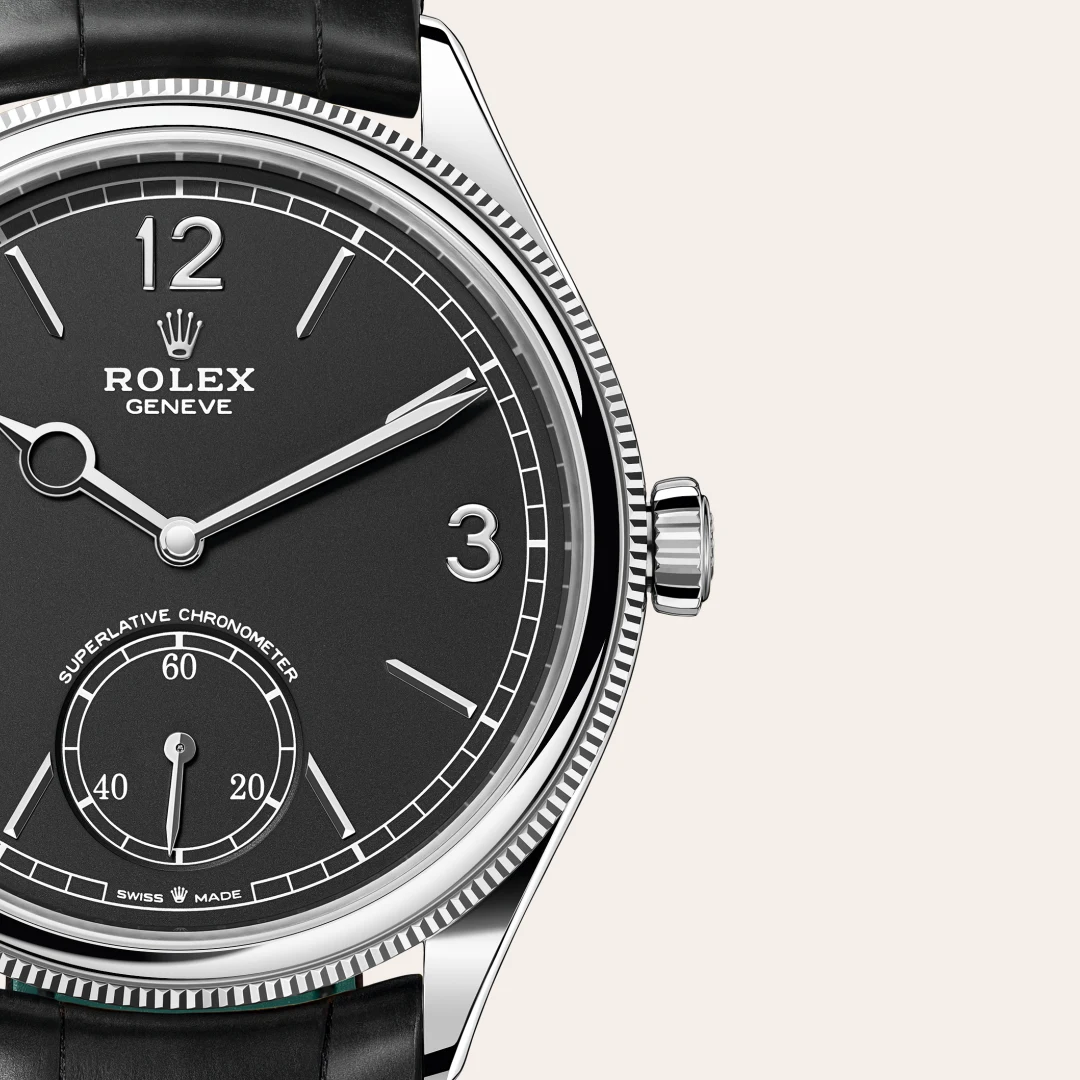m52509-0002-slide3 | Brela Close-up of a Rolex wristwatch face: black dial, silver hands, crown, and subdial with leather strap visible. | Brela