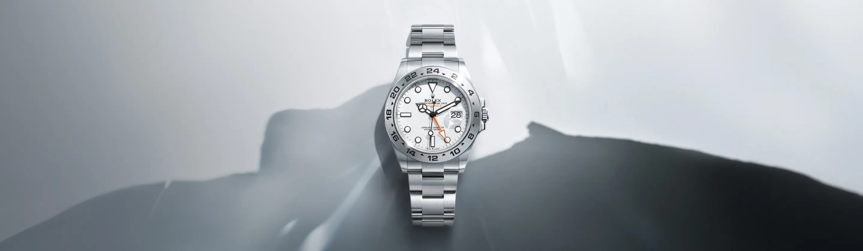 Stainless steel Rolex wristwatch with a white dial and date window against a gray, abstract mountain backdrop.