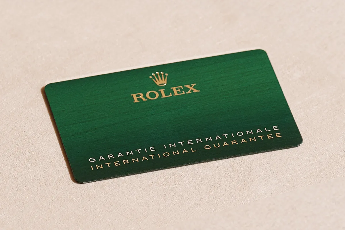 Green Rolex warranty card with gold crown logo and text on a beige surface.