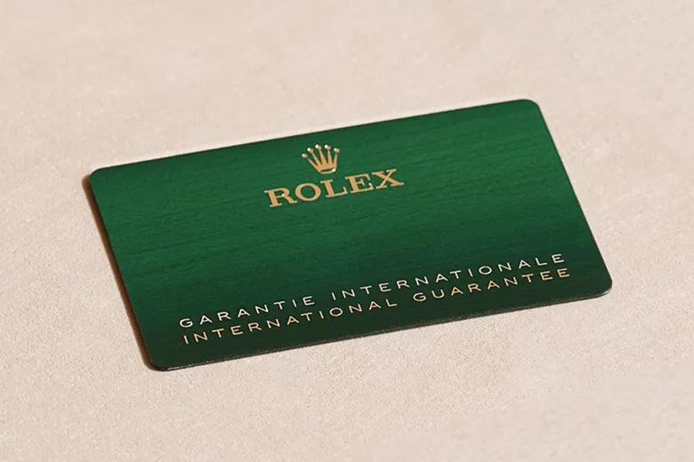 Green Rolex warranty card on a beige surface with gold lettering and crown logo at top.