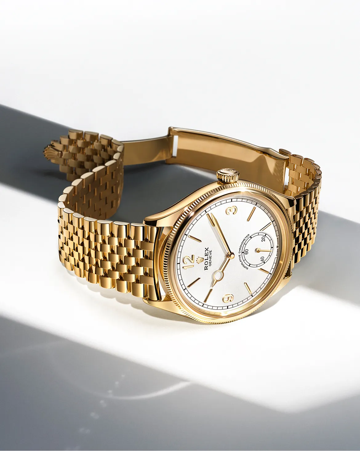rolex-oyster-perpetual-universal-classic-style-m52508-0008_portrait Gold Rolex wristwatch with white dial and gold bracelet resting on a white surface.