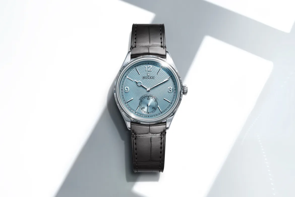 rolex-perpetual-1908-cover-m52506-0003-portrait Rolex wristwatch with a light blue textured dial and black leather strap on a white surface.