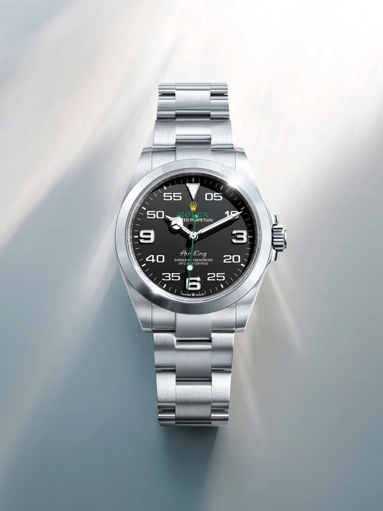 rolex-watches-air-king-m126900-0001-portrait | Brela Stainless steel wristwatch with a black dial and bold white numerals on a metal bracelet, angled against a reflective background. | Brela