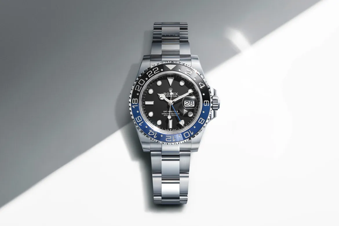 rolex-watches-gmt-master-ii-m126710grnr-0003-landscape | Brela Rolex GMT-Master II stainless steel watch with black dial, blue/black bezel, and date window at 3 o'clock on a two-tone background. | Brela