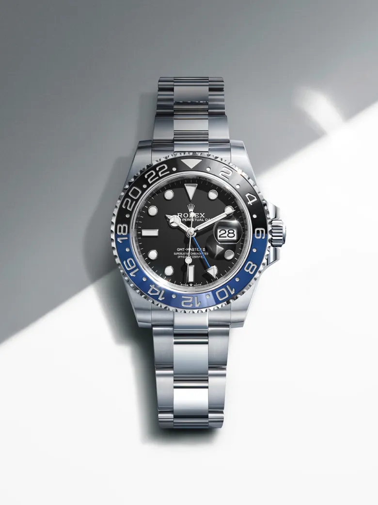 rolex-watches-gmt-master-ii-m126710grnr-0003-portrait | Brela Rolex GMT-Master II wristwatch with a black dial, blue and black bezel, and stainless steel bracelet, showing the date at 3 o'clock on a gray background. | Brela