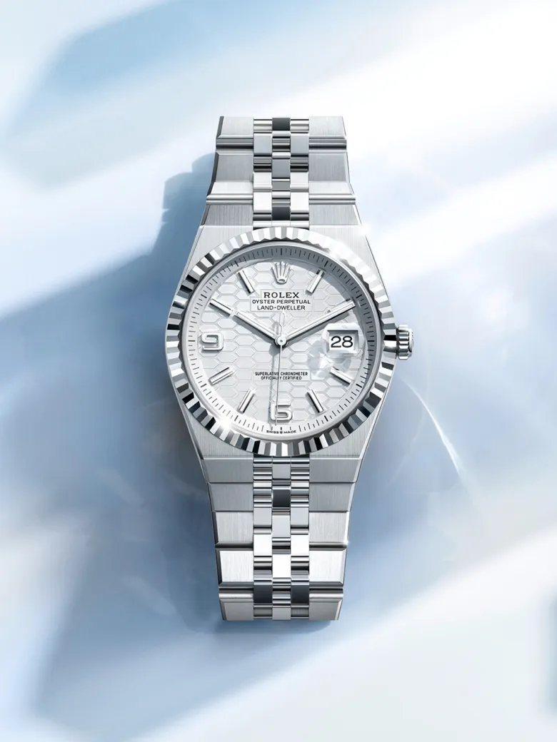 rolex-watches-land-dweller-m127234-0001-portrait | Brela Silver Rolex Oyster Perpetual Land-Dweller in stainless steel with fluted bezel and date window at 3, on a pale blue background. | Brela