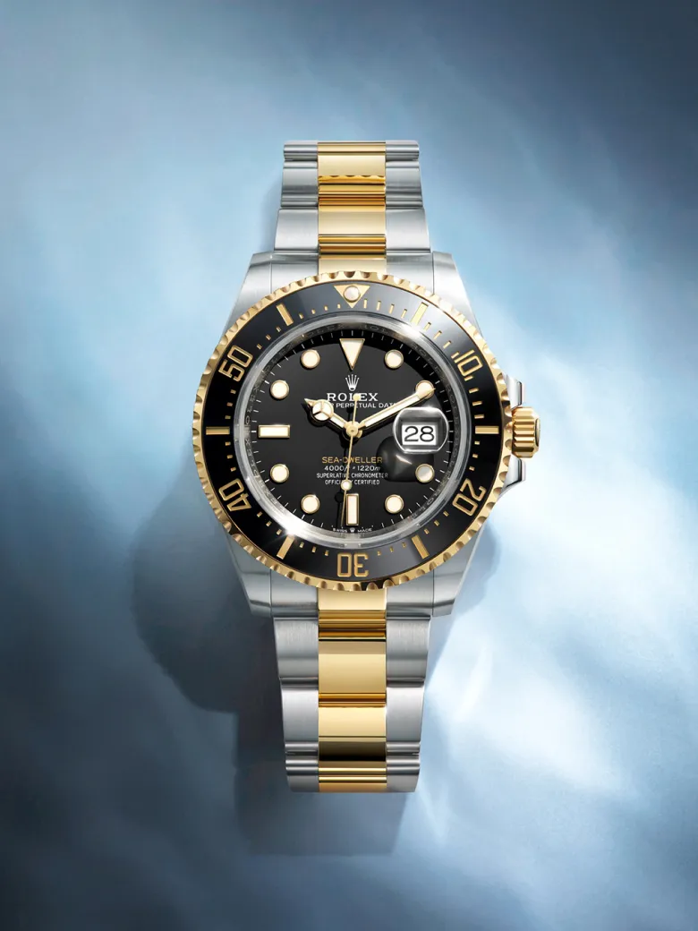 rolex-watches-sea-dweller-m126603-0001-portrait | Brela Two-tone Rolex Sea-Dweller watch with black dial, gold bezel, and steel-and-gold bracelet showing date magnifier at 3 o'clock | Brela