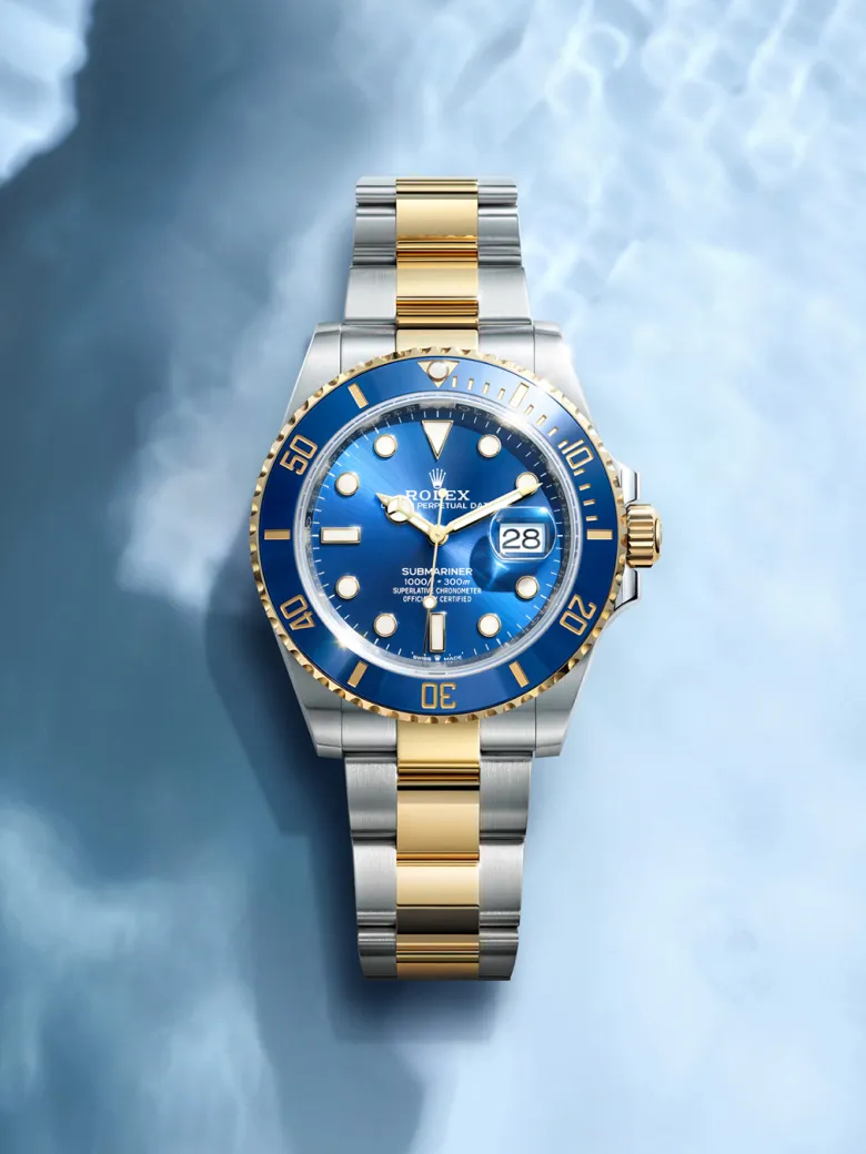 rolex-watches-submariner-m126613lb-0002-portrait | Brela Rolex Submariner two-tone watch with a blue dial and date window, laid on a light blue surface | Brela