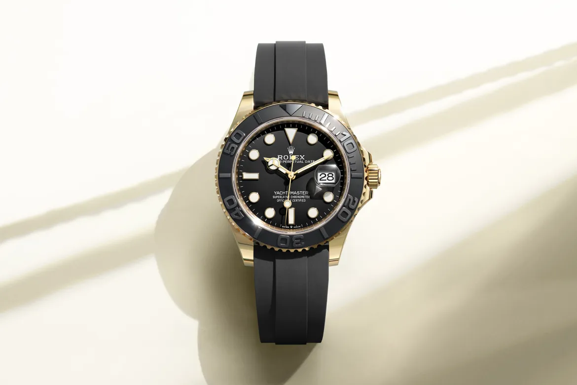 rolex-watches-yacht-master-m226658-0001-landscape | Brela Rolex Yacht-Master watch with black dial, gold case, and black rubber strap on a light background, showing date at 3 o'clock. | Brela