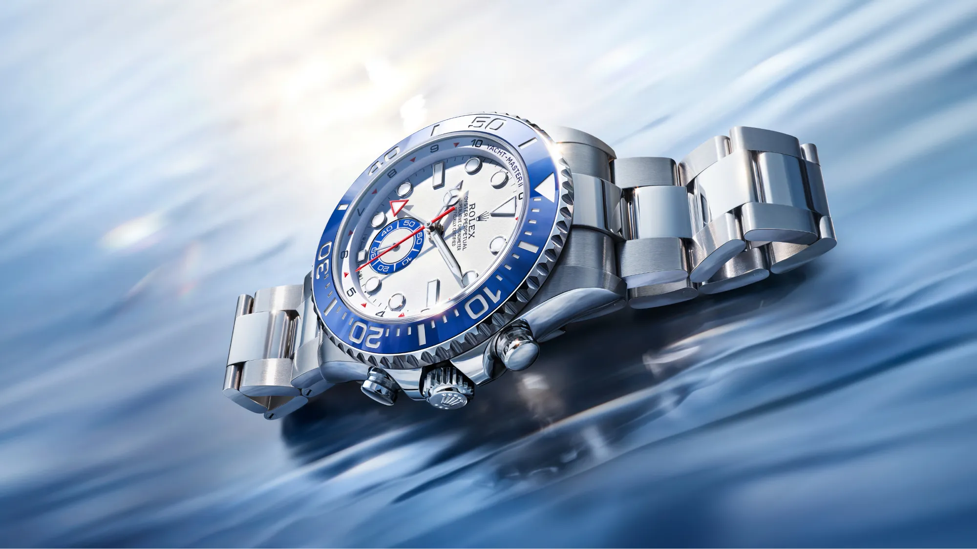 Close-up of a silver Rolex wristwatch with a blue bezel, angled on a blurred blue background, showing the Rolex logo on the dial.