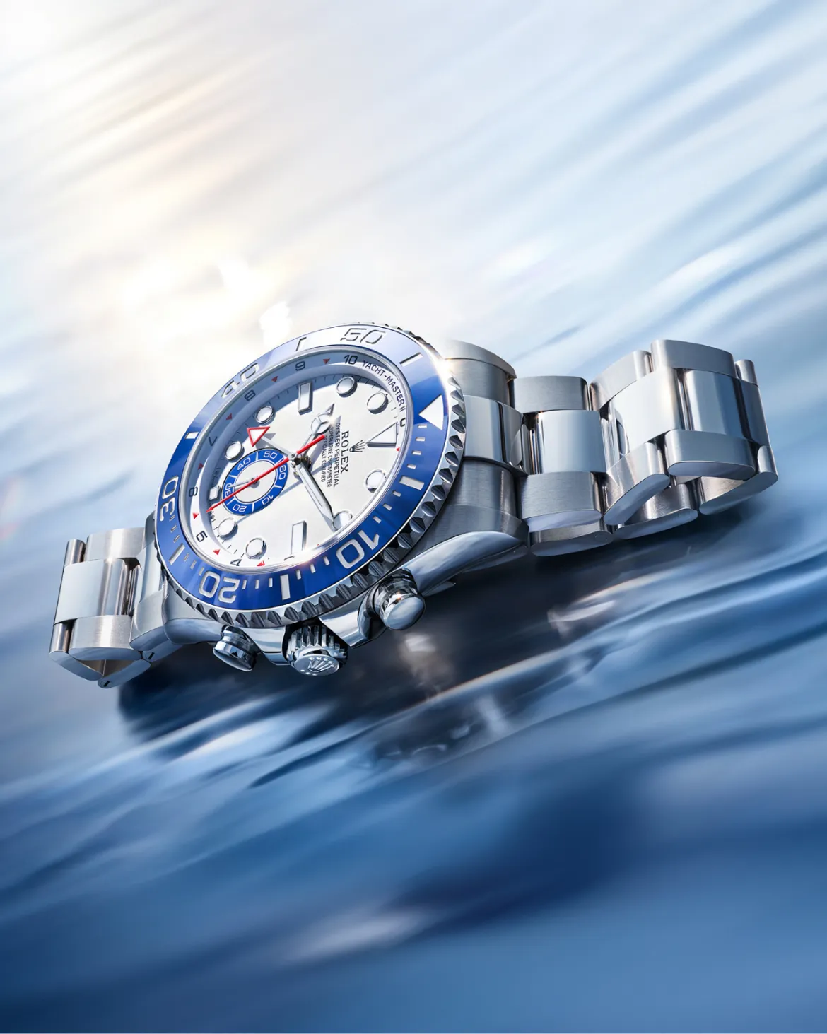 Stainless steel Rolex Yacht-Master watch with a blue bezel resting on a glossy blue surface