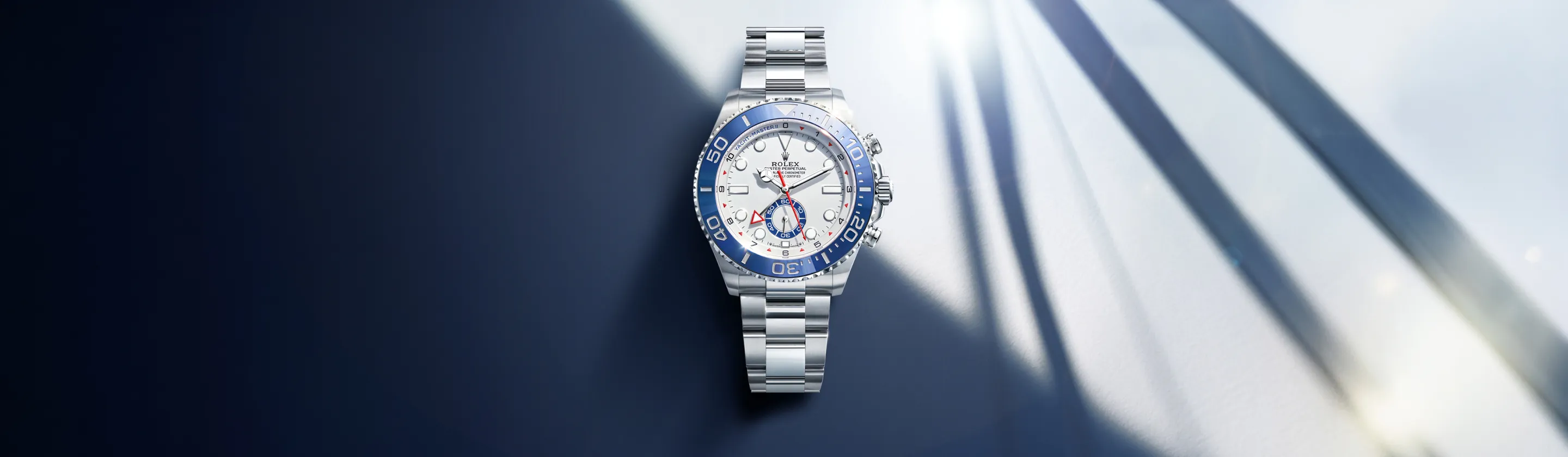 Stainless steel Rolex watch with a blue bezel and white dial resting on a dark blue surface.