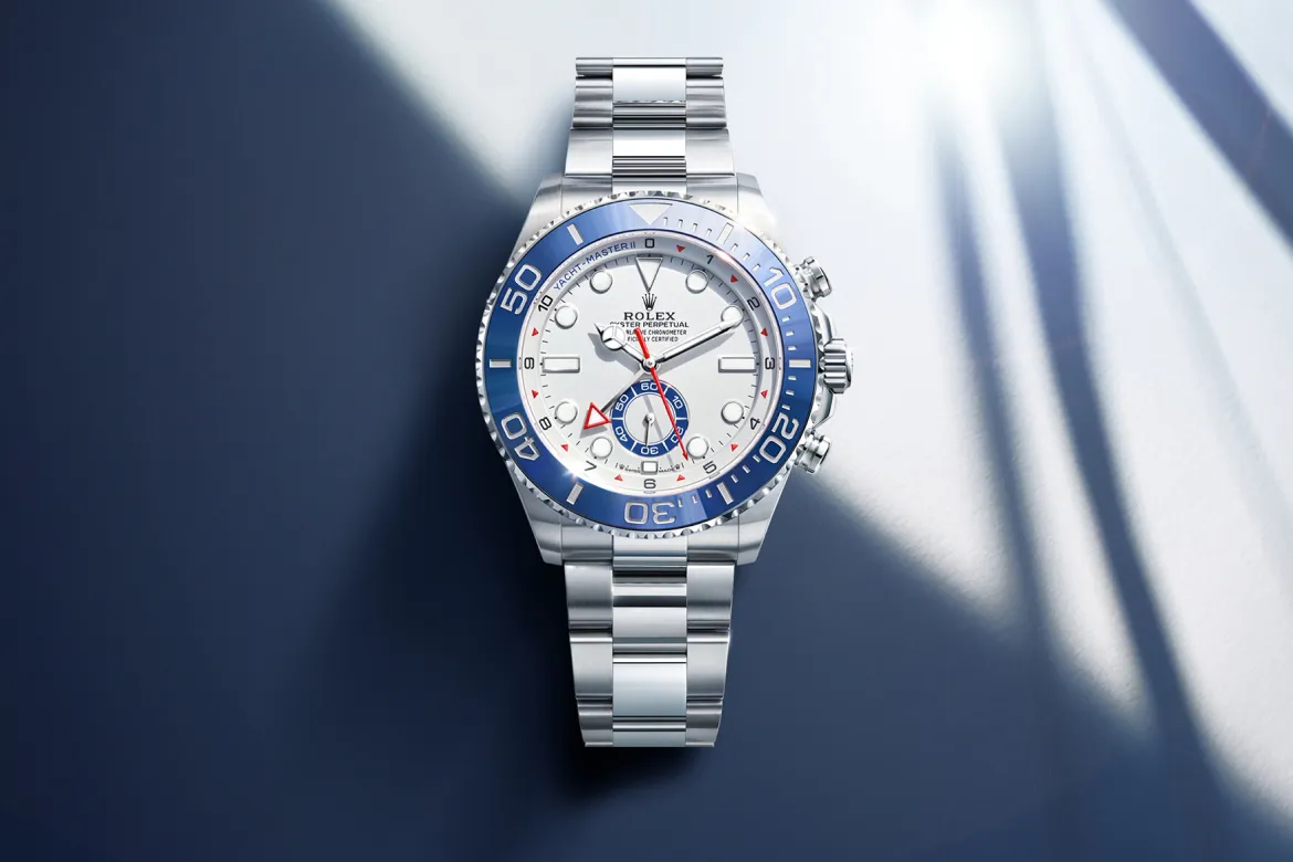 Stainless steel Rolex Yacht-Master II watch with white dial and blue bezel on a blue surface.
