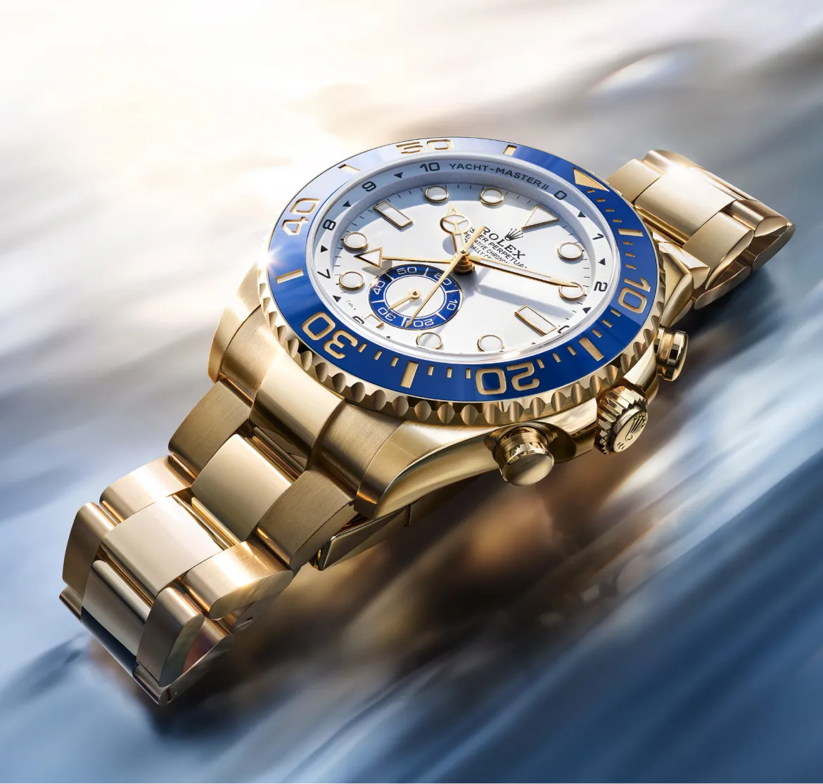 Gold Rolex Yacht-Master II wristwatch with blue bezel lying on a reflective surface; luxurious nautical design