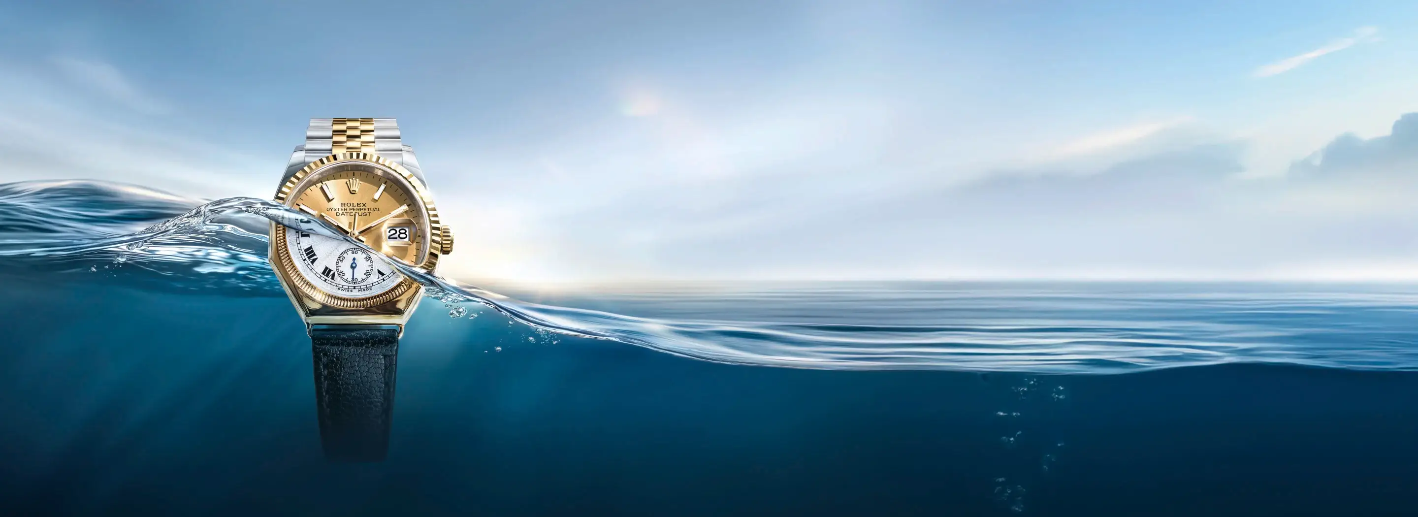Gold Rolex watch partially submerged in blue ocean with a splash and clear sky behind it.