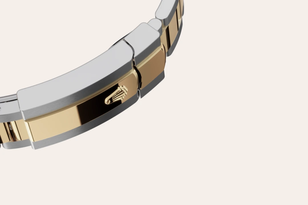 Close-up of a two-tone gold and silver watch bracelet with a clasp featuring a crown emblem on the gold panel. | Brela