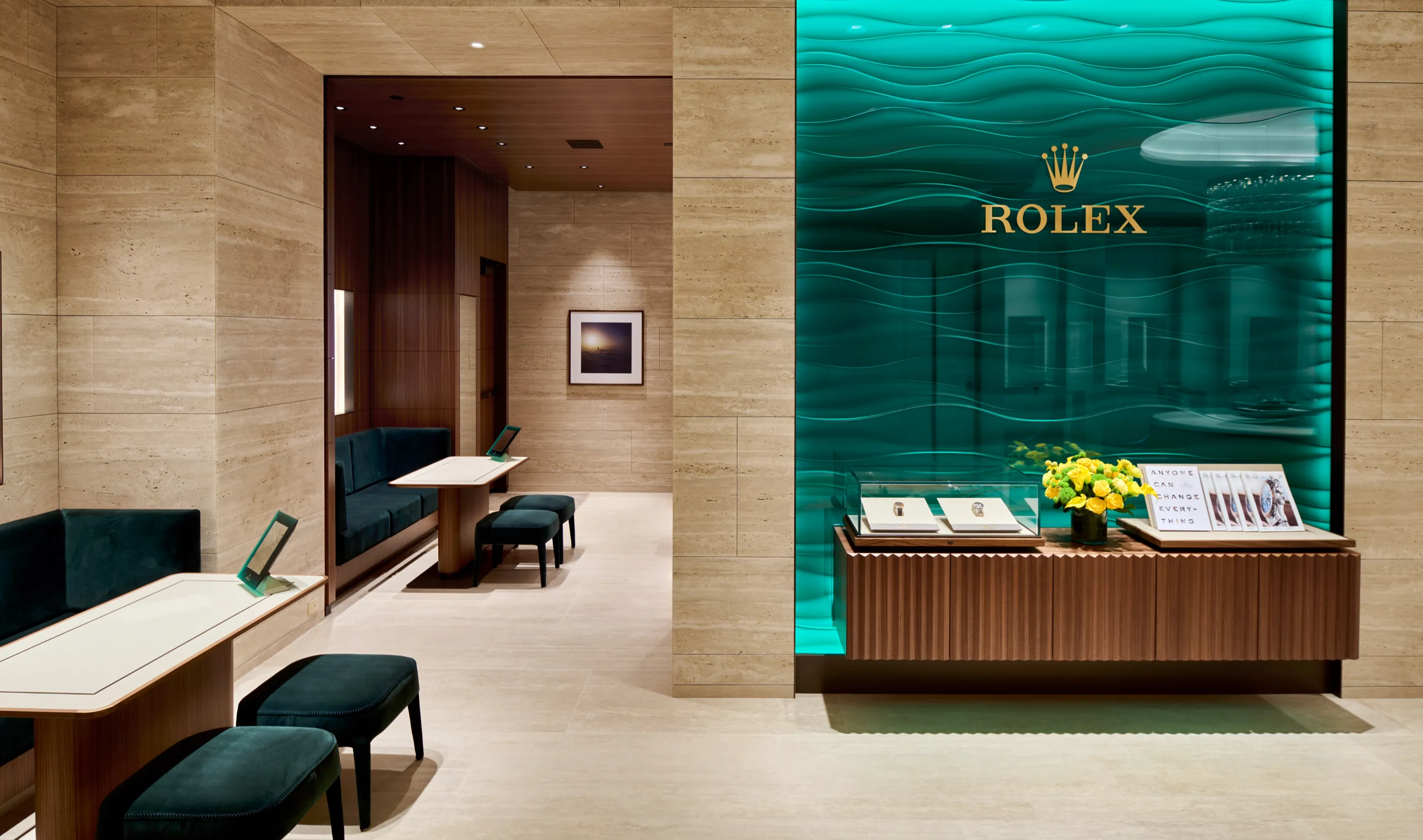 rolex-contact-rolex-bloor-robert-lowdon-photography-0007_r-landscape | Brela Interior of a Rolex showroom featuring beige stone walls, a teal glass display with the Rolex logo, and a wooden display counter with jewelry and flowers. | Brela